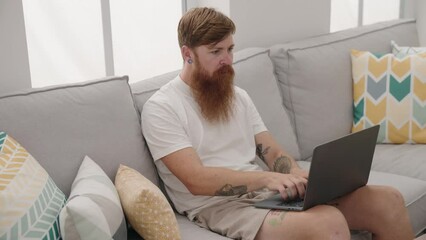 Sticker - Young redhead man using touchpad sitting on sofa at home