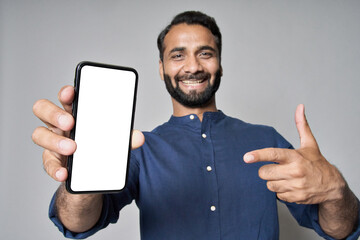 Happy indian business man standing isolated on grey holding cellular pointing at mobile phone showing mockup white big cellphone screen advertising smartphone technology applications.