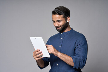 Happy smiling indian business man employee or manager standing isolated on gray background holding using digital tablet advertising online product, business trainings webinars, websites or services.