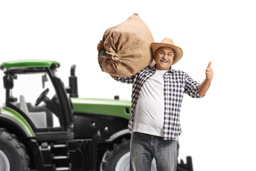 Wall Mural - Mature farmer with a sack gesturing thumbs up in front of a tractor