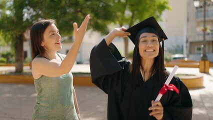 Poster - Two women mother and daughter throwing graduated hat to the sky at park