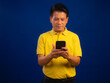 © kobps2 - Portrait of smart middle-aged asian man in casual yellow T-shirt holding smartphone isolated on blue background in studio, looking happiness and attractive