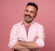 Smiling man posing with arms crossed on pink background. Portrait of attractive handsome mature man in rose shirt with crossed arms. Healthy happy smile senior beard caucasian man isolated on pink.