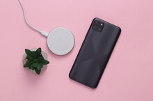 Modern Smartphone With Wireless Charging Platform And Decorative Plant, Pink Background. Modern Gadgets. Top View, Flat Lay
