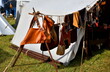 A close up on a display of cloth and leather equipment of medieval peasants, nobility, and knights hanging from a sturdy rope next to a cloth tent seen during a medieval fair in Poland