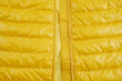 A bright background of a shortened yellow down jacket with an unbuttoned zipper. Quilted jacket for autumn or winter. The concept of a seasonal sale of warm outerwear. View from above.
