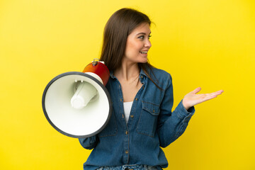 Young caucasian woman isolated on yellow background holding a megaphone and with surprise facial expression