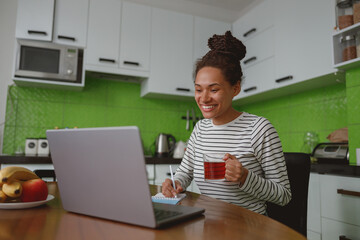 Wall Mural - joyful positive female freelancer working online on laptop during breakfast drinking tea