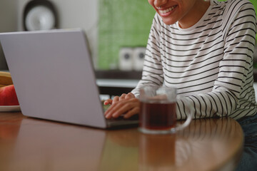 Wall Mural - smiled happy female sitting at table at home and texting on laptop searching internet