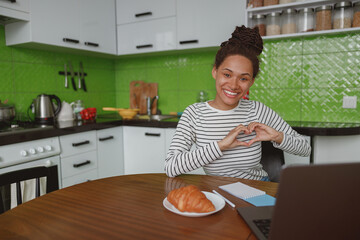 Wall Mural - portrait of happy mixed-race female smiling to camera and showing love gesture indoor