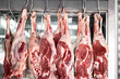Raw mutton or lamb legs hanging on butcher hooks