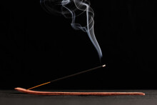 Smoke Curls Of Burning Incense Stick In Wooden Holder For Relaxation And Meditation Black Background