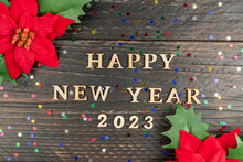 Happy New Year 2023 Celebration. Wooden Text And Poinsettia On Wooden Background. Flat Lay.
