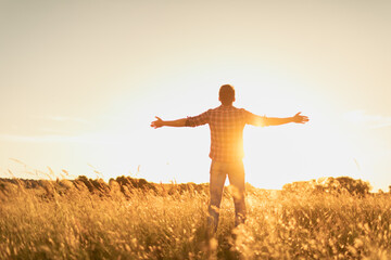 Happy person in the field at sunset. Young man feeling free energized in nature.