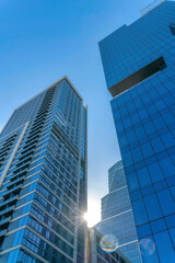 Wall Mural - Skyscrapers with glass windows facade against bright sun and clear blue sky