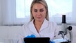 © Евгения Медведева - Woman scientist research chemist in a medical suit and protective gloves with a tablet computer and a microscope conducts research in the laboratory.