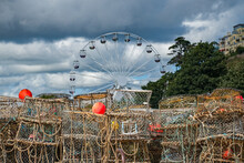 Crab Pots At A Harbor In Sharp Focus. A Big Wheel Behind In Soft Focus Contrasts Industry Against Leisure. Colorful And Highly Detailed.