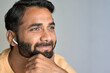 Thoughtful smiling bearded indian man relaxing wearing earbud thinking while listening to music, business podcast or audio book in mobile application isolated on gray. Close up portrait. Copy space