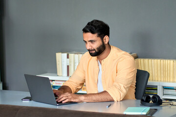 Busy indian business man employee, eastern professional manager using laptop computer in office online working on digital tech project management doing marketing operations or crypto trading analysis.