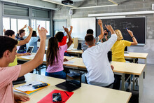 Group Of High School Students Raising Hands In Classroom - Education Concept