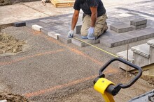 Landscaping Contractor Worker Using Tape Measure Ruler Measuring And Laying Interlock Stones On A Construction Site. 