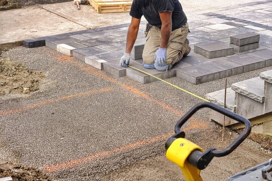 landscaping contractor worker using tape measure ruler measuring and laying interlock stones on a co