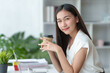 © amnaj - At the office, a young Asian businesswoman sit and relaxe with a cup of coffee and a bright smile on her laptop.