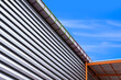 Aluminum louver wall with steel rain gutter and arcade roof outside of warehouse building against blue sky background