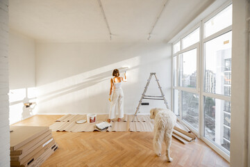 Wall Mural - Woman with her dog paints the wall in white color, making repairment in newly purchased apartment. Repair and house renovation concept