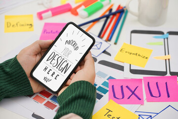 Wall Mural - creative ux ui designer hand holding mobile white screen mockup at working desk space. white screen 