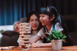 © Kiattisak - Asian happy family of little daughter play toy wooden block in home. Mother or mom young woman loving parent having fun play stack tower wood block game at night in living room. Hobbie leisure concept