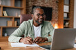 © Prostock-studio - Smiling middle aged african american male in glasses and casual working on laptop in home office interior