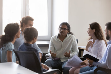 Indian man speaking on group therapy meeting, sharing story, problem. Business team sitting on chairs in circle, talking, discussing solutions, project ideas, brainstorming