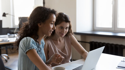 Poster - Two diverse employees working on project tasks together, sharing laptop, watching online presentation, making video call. Company teacher training intern. Business communication concept