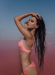 Wall Mural - beautiful woman with dark hair in elegant swimmng suit posing on the pink salt lake