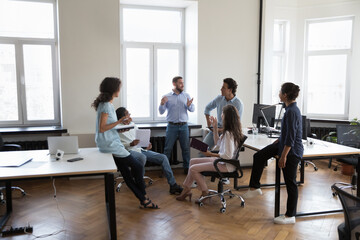 Canvas Print - Happy confident business leader man motivating team, presenting ideas for project, speaking before coworkers in office space. Mentor training diverse group of interns