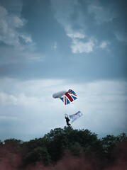 Wall Mural - Vertical shot of a parachute with a flag of Great Britain flying over the trees