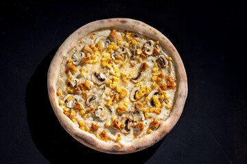 Appetizing pizza on a creamy sauce with mushrooms, corn, chicken fillet and mozzarella cheese on black background