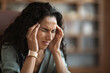© Prostock-studio - Stressed woman suffering from headache, touching her head, office interior
