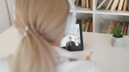 Wall Mural - Online education. Female student. Foreign courses. Unrecognizable woman in headphones having virtual meeting on tablet computer in light room interior.