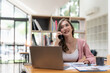 © Natee Meepian - Attractive young female having smartphone conversation in modern library. Financial accounting concept.