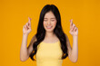 Cheerful happy young asian woman makes attempt to wish good luck crossed fingers, has better faith standing over yellow background Smilling girl holding .her finger crossed for good luck and eye close