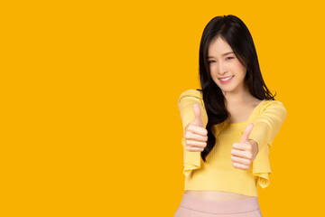 Smiling beautiful Asian woman showing thumbs up isolated on yellow background and copy space Grinning glad accept plan Cheering to you Congratulate good job Approving good idea Like nice outfit