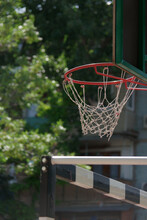 View Of Red Metal Basketball Hoop With White Net And Backboard Against The Green Park Trees And Nearby Handball Goal
