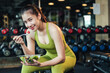 © ME Image - Beautiful asian woman in sportswear healthy eating salad after exercise at fitness gym. Healthy lifestyle. Young female smiling with holding salad bowl and looking at camera.