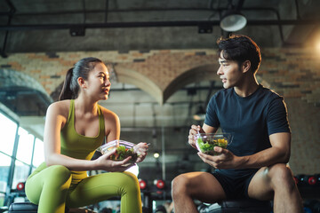 two asian people healthy eating salad after exercise at fitness gym. asian man and woman eating sala