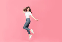 Young Asian Woman In A White T-shirt Cheerful Expression On Her Face As She Is Very Happy Over Something Excited Smile And Jumping With Her Arm Raised In Air On Isolated Pink Background.
