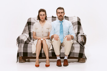 Wall Mural - Portrait of serious man and woman sitting on sofa and looking at camera isolated over white background