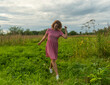 © Dmitry - a girl in a red dress runs through a meadow with green grass