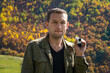 © yaroslav1986 - Portrait of a young male blogger with an action camera against the background of mountains on a sunny autumn day.Man with pursed lips looks into the camera against background of an autumn landscape